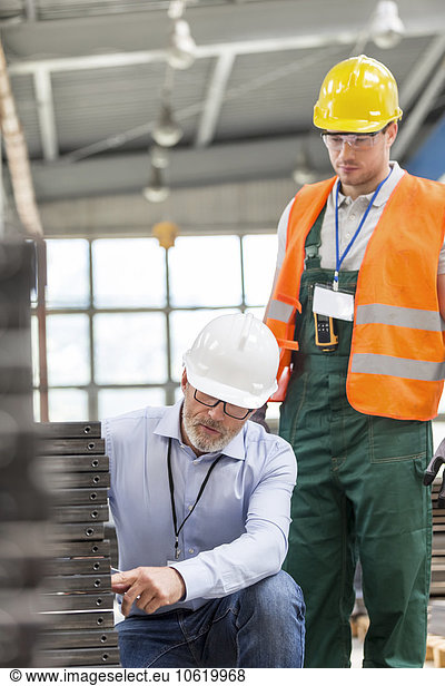 Engineer explaining steel parts to worker in factory