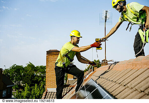 Engineer giving drill machine to colleague on roof