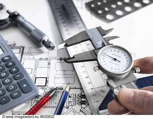 Engineer holding dial caliper with measurement equipment sitting on technical drawing