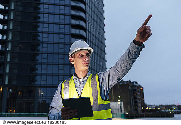 Engineer holding tablet PC pointing in front of building