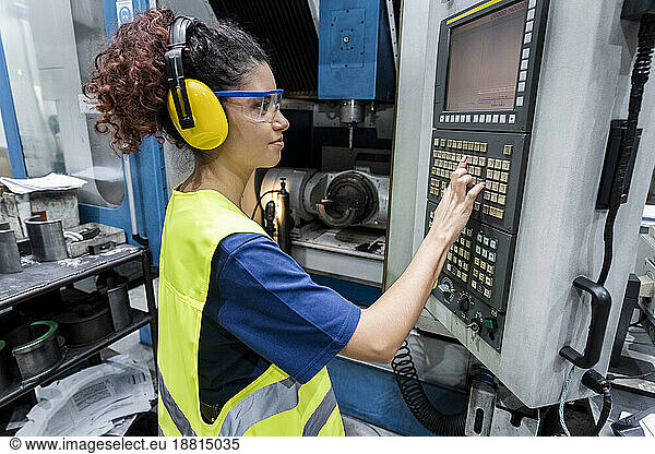 Engineer in protective workwear operating CNC machine in modern factory