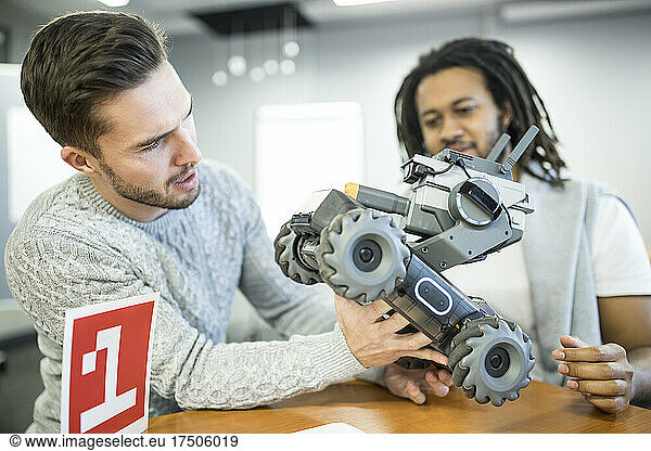 Engineer looking at robotic combat tank with colleague at workshop