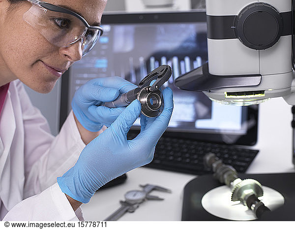 Engineer measuring manufactured component for accuracy and quality control using a dial caliper  3D stereo microscope in background