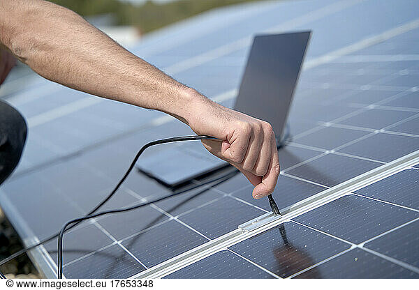 Engineer plugging in power supply cable charger of laptop to solar panels