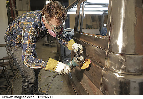 Engineer polishing van with angle grinder in factory