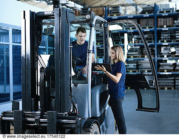 Engineer showing tablet PC with worker in forklift at factory