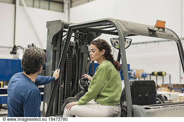 Engineer sitting in forklift discussing with colleague at factory