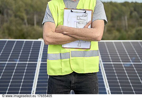 Engineer standing in front of solar panels with blueprint