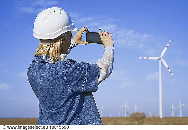 Engineer taking picture of wind turbine through smartphone