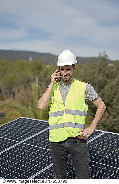 Engineer talking on mobile phone standing in front of solar panels on sunny day