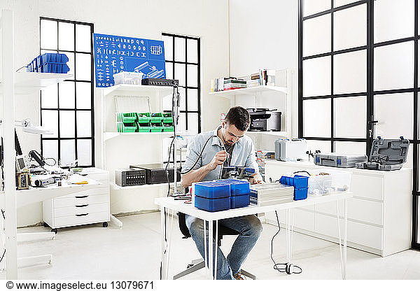 Engineer using drill on circuit board at table in electronic laboratory