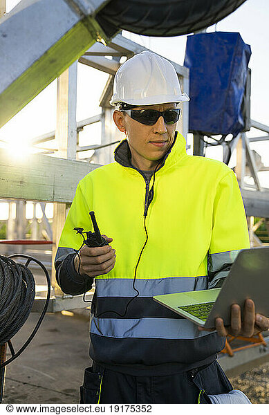 Engineer using laptop and walkie-talkie by wind turbine maintenance machine