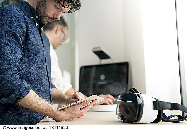 Engineer using tablet computer while colleague using computer in office
