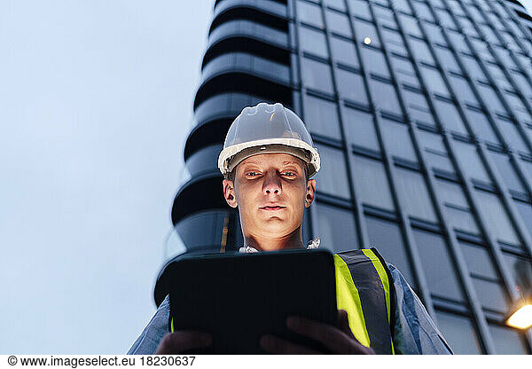 Engineer using tablet PC in front of building at dusk