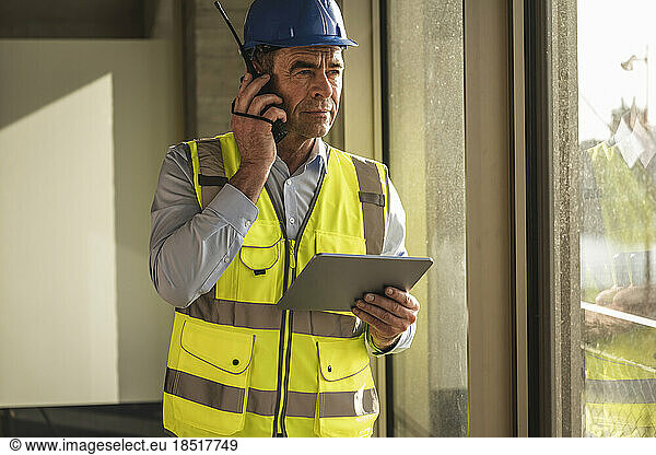 Engineer using walkie talkie standing with tablet PC in office