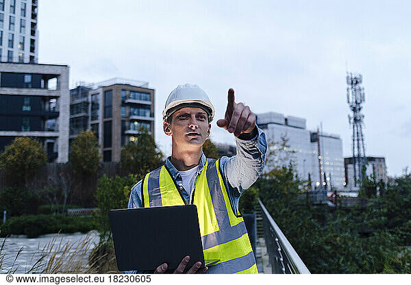 Engineer wearing hardhat pointing and holding laptop