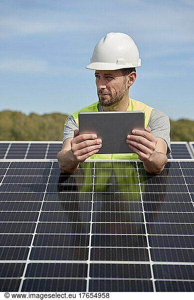 Engineer wearing hardhat using tablet PC between solar panels on rooftop