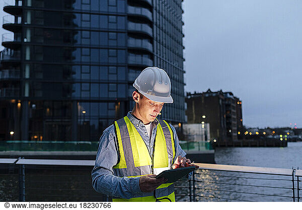 Engineer wearing hardhat using tablet PC by railing