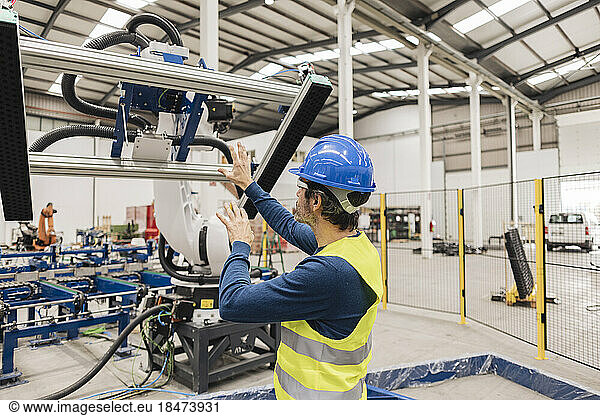 Engineer wearing protective work wear examining machine part in factory