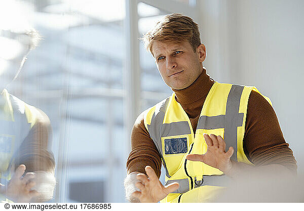 Engineer wearing reflective clothing gesturing in office