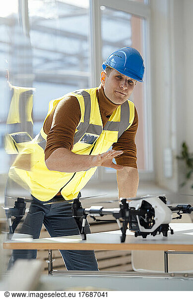 Engineer wearing reflective clothing gesturing with drone at desk in office