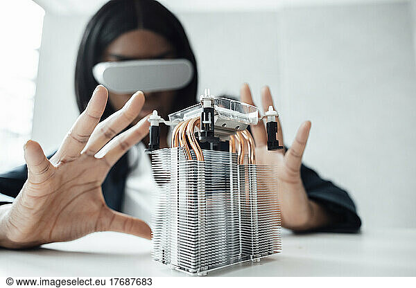 Engineer wearing virtual reality simulator gesturing at machine part on desk