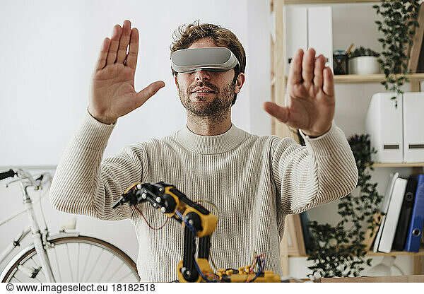 Engineer wearing VR goggles working on robotic arm in office