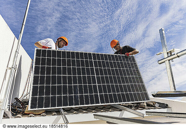Engineer with colleague holding solar panel on roof