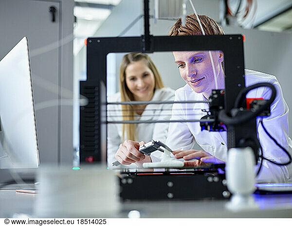 Engineer with colleague operating 3D printing machine in laboratory