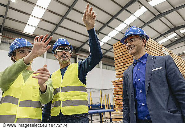 Engineer with colleague wearing smart glasses gesturing at transparent screen in factory