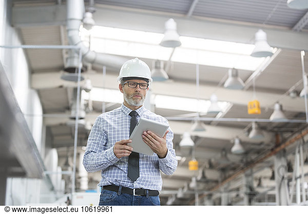Engineer with hard-hat and digital tablet walking in factory
