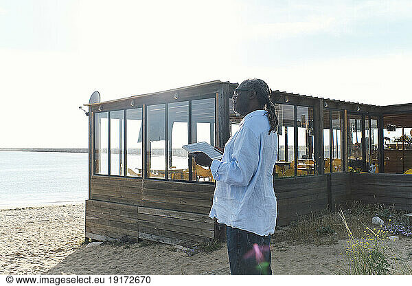 Engineer with solar panel standing in front of cafe at beach