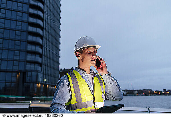 Engineer with tablet PC talking on smart phone at dusk
