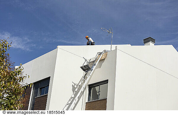 Engineer working on roof of house under sky