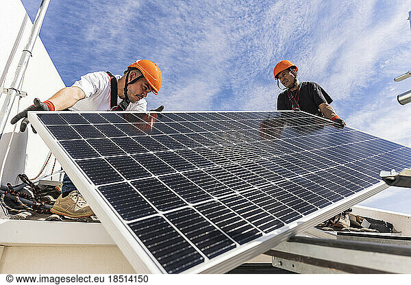 Engineers holding solar panel on roof