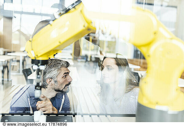 Engineers pointing at industrial robot in glass talking to colleague
