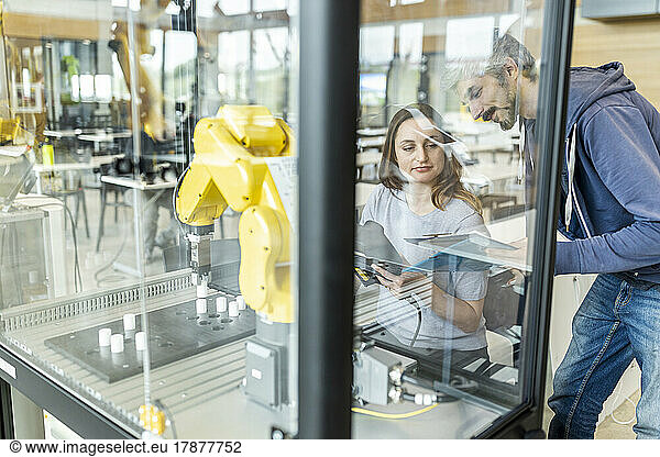 Engineers testing industrial robot in glass cabin