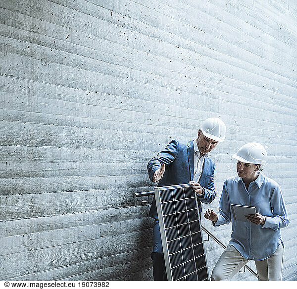 Engineers wearing hardhat and discussing over solar panel at site