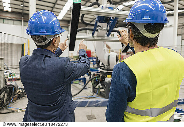 Engineers wearing hardhat examining machine part