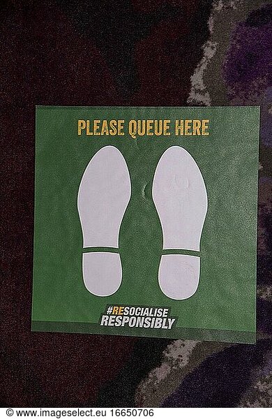 England  Ein Please Queue Here -Schild auf dem Teppich eines Hotels im Vereinigten Königreich. Während der Coronavirus-Epidemie.