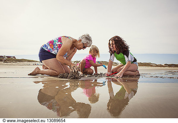 Enkelinnen mit Großmutter graben kniend im Sand am Strand