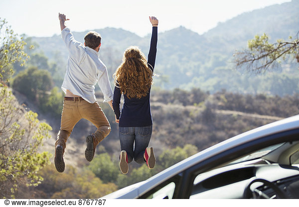 Enthusiastic couple jumping for joy outside car