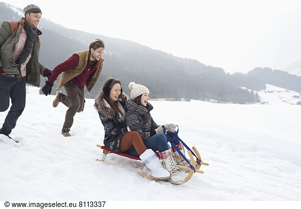Enthusiastic friends sledding in snowy field