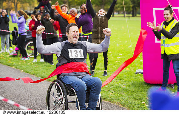 Enthusiastic man in wheelchair crossing finish line at charity race in park
