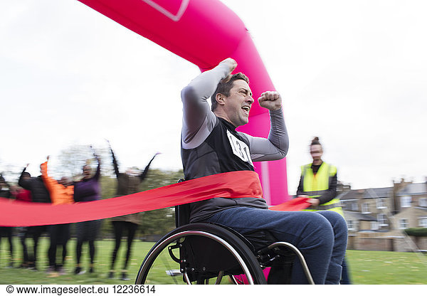Enthusiastic man in wheelchair crossing finish line  cheering at charity race in park