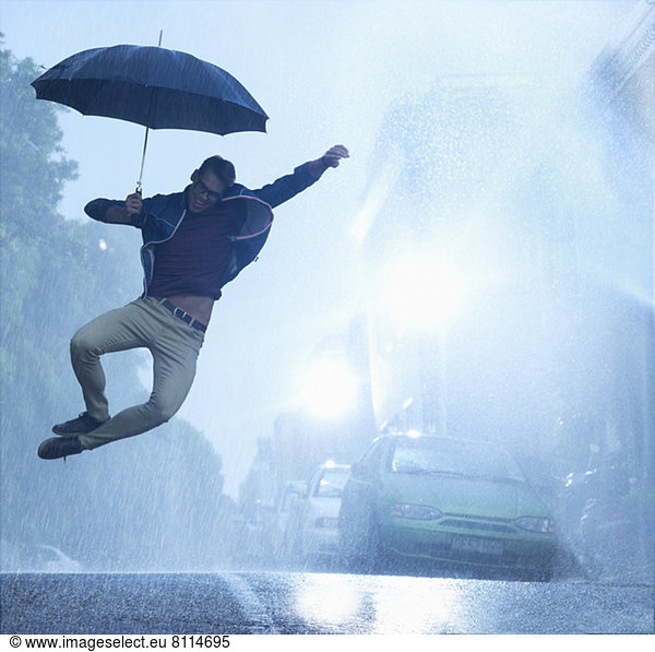 Enthusiastic man with umbrella jumping in rain