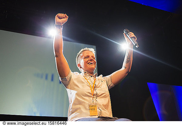 Enthusiastic  smiling female speaker with microphone cheering on stage