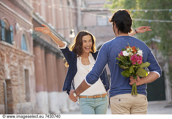 Enthusiastic woman approaching man with flowers behind back