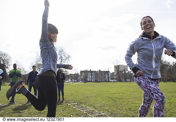 Enthusiastic woman cheering for teammate doing speed ladder drill in park