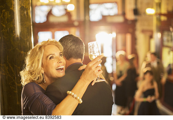 Enthusiastic woman with champagne hugging man in theater lobby